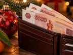 Купюры по 5000 рублей в кошельке рядом с ёлочной игрушкой и мандарином